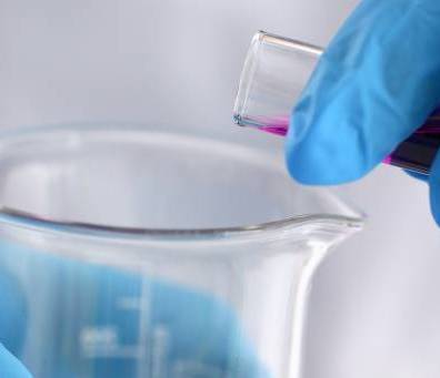 Image of chemist's hand emptying a vial into a beaker