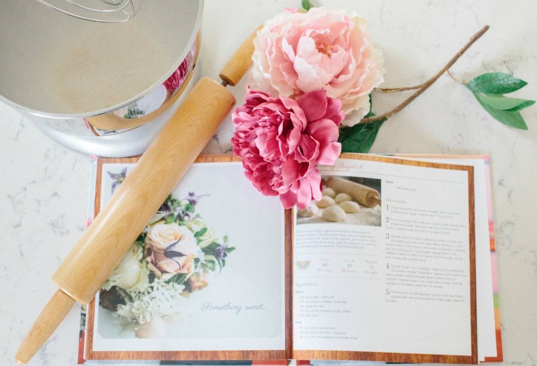 flat lay of cookbook with cooking utensils and flower
